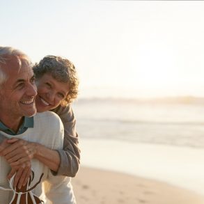 Portrait of happy mature man being embraced by his wife at the beach. Senior couple having fun at the sea shore.
