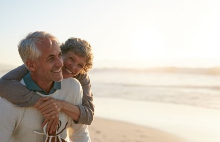 Portrait of happy mature man being embraced by his wife at the beach. Senior couple having fun at the sea shore.