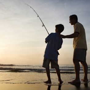 Man and young boy fishing in surf