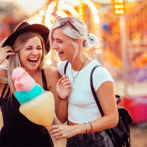 Two girls having cotton candy at an amusement park.