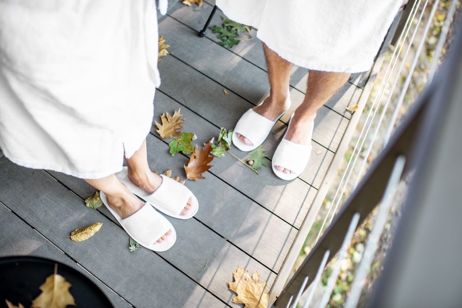 Couple in bath robe and slipppers standing on the terrace with beautiful leaves outdoors. View from above with no face