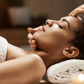 Attractive african girl enjoying face massage in spa salon.
