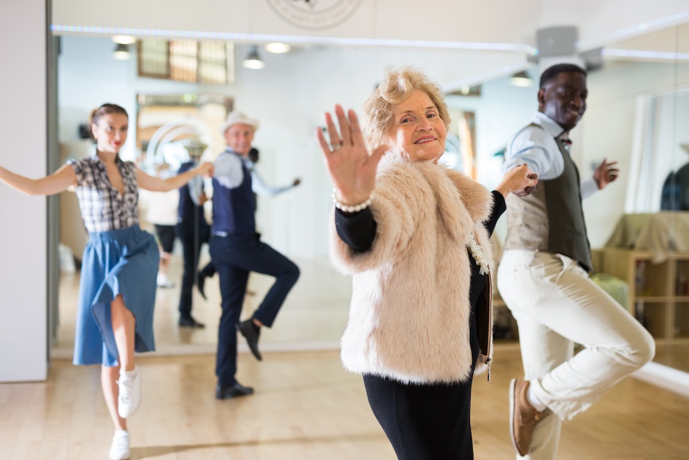Portrait of a mature dancing woman at a group training session, practicing an energetic swing in pair in studio of dance